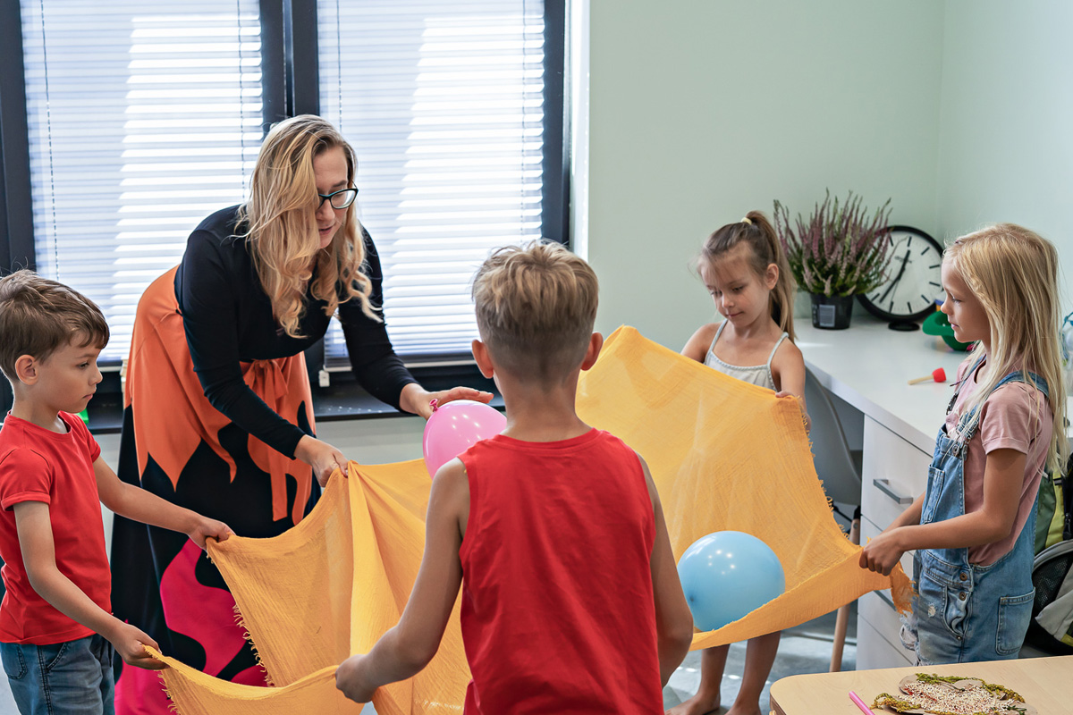 kobieta i czwórka dzieci trzymają koc na którym są kolorowe balony